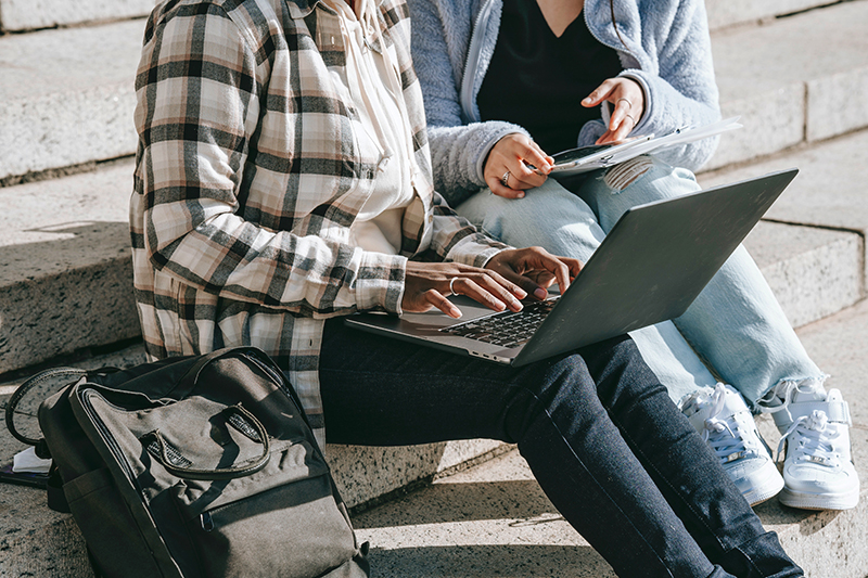 Business Personen die arbeiten, dazu ein bei gelegter Fahrradtasche-Rucksack. Zwei Personen die an einem Laptop sitzen, mit der Fahrradtasche-Rucksack im Vordergrund.