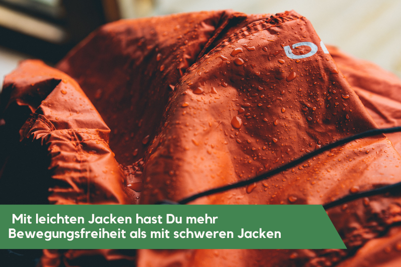 Orange Regenjacke, in Grossaufnahme. Das Wasser perlt an der Jacke ab